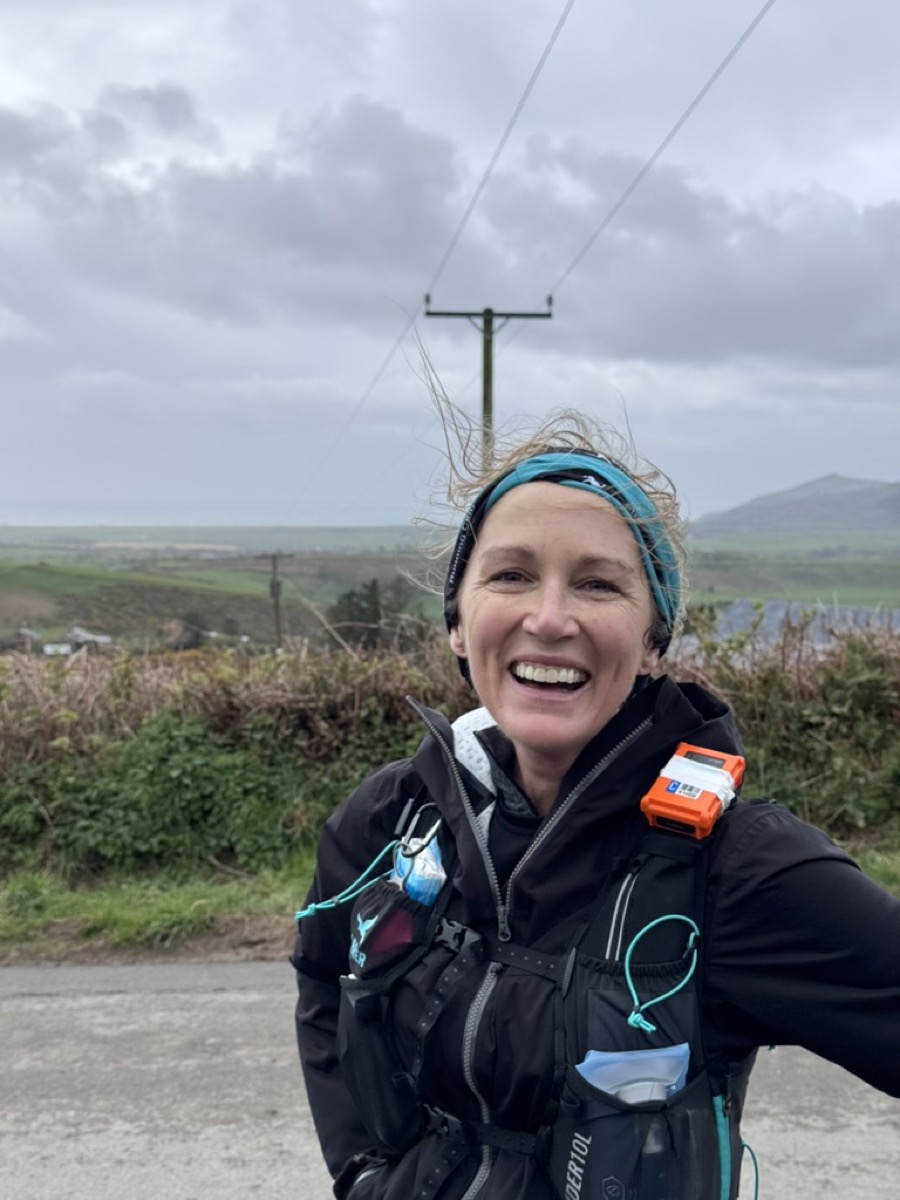 Cass smiling on the course with wind in her hair and the Welsh hills behind her