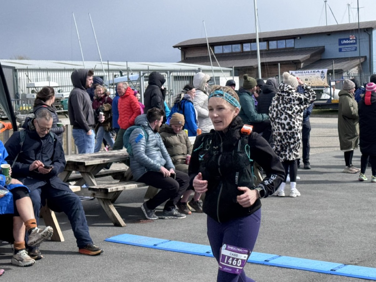 Cass crossing the She Ultra finish line, bib 1460, RNLI station in the background